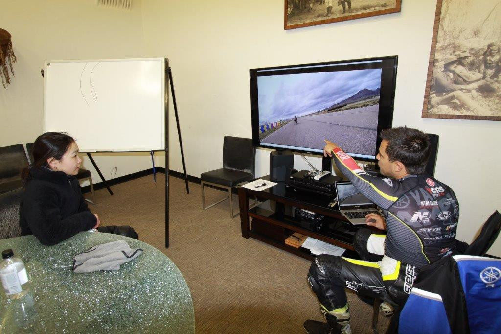 Chris Peris reviews some on-track video with Hiyori Yoshida. He is pointing out how in a double-apex turn she is looking to the second apex and then turning too early, instead of looking for the outside curbing to achieve a more proper line through the second apex. Photo by Army Of Darkness Ministry of Information.