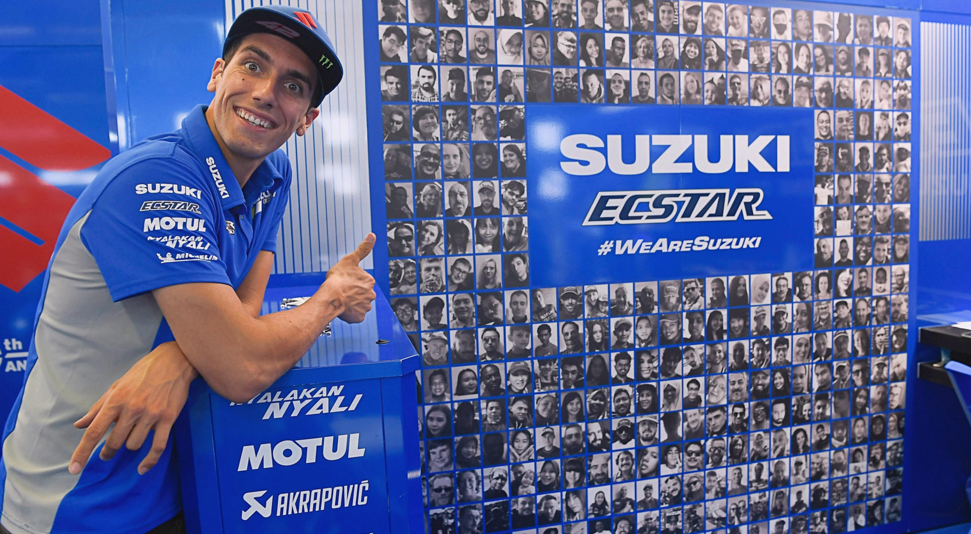 Alex Rins in front of a huge vinyl collage of fans' photos in the Team Suzuki ECSTAR pit box at Misano. Photo courtesy Team Suzuki Press Office.