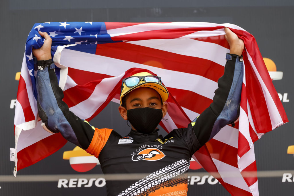 American Kristian Daniel Jr. standing on the podium holding an American flag at Motorland Aragon. Photo by Rafa Morrodan, courtesy Noyes Camp Academy.