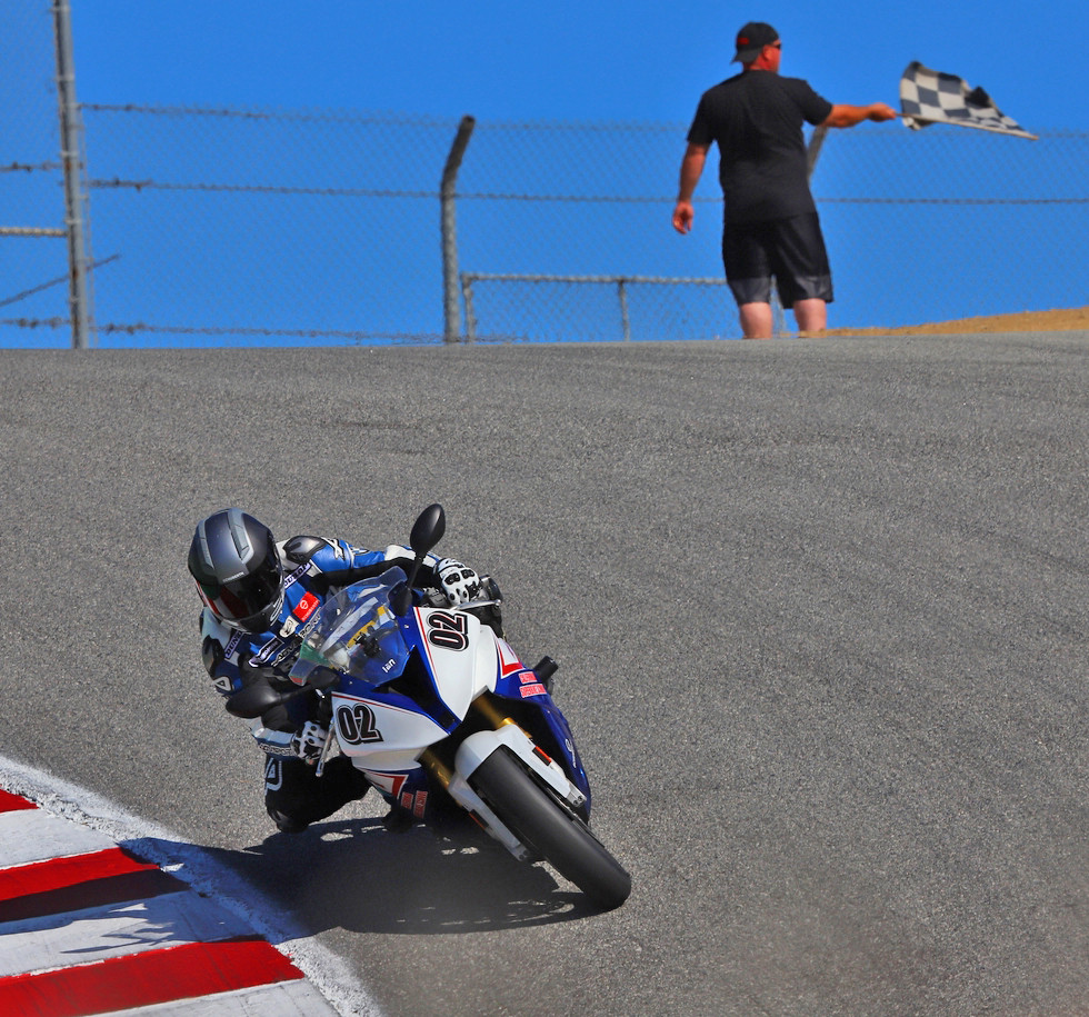 A California Superbike School instructor takes the checkered flag at the Corkscrew at Laguna Seca. Photo by etechphoto.com, courtesy California Superbike School.