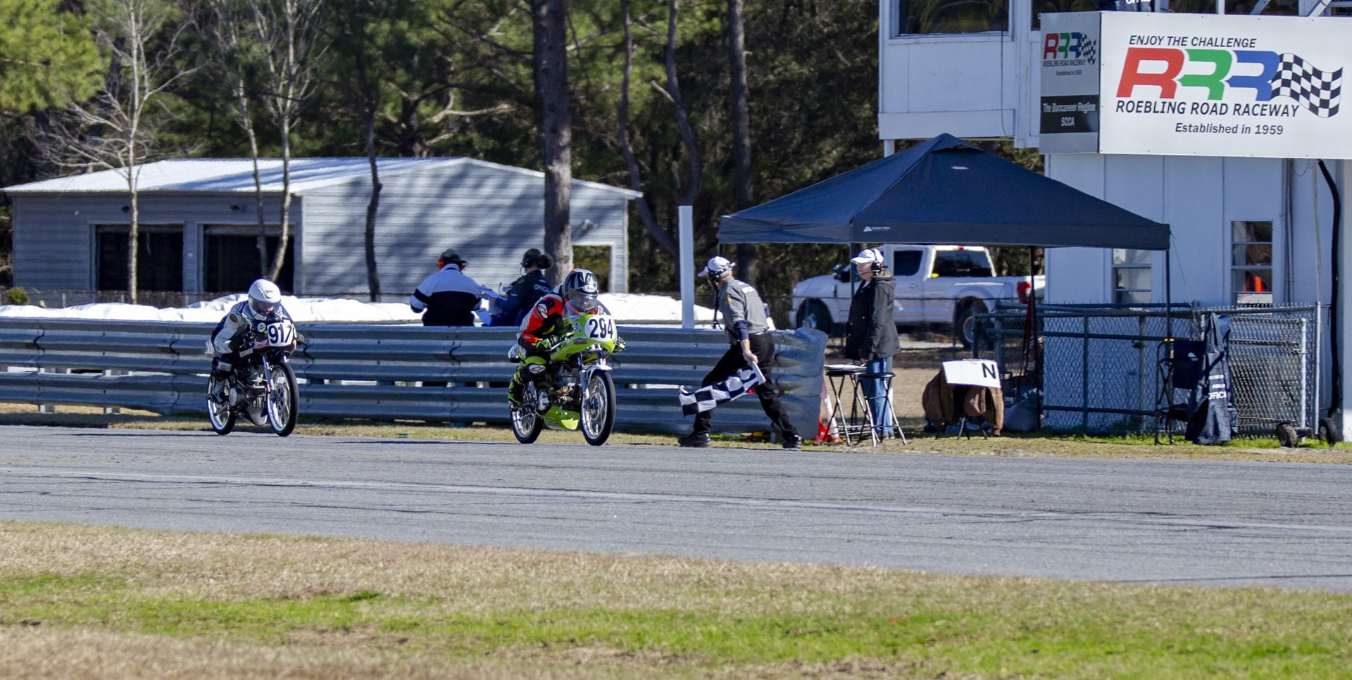 AHRMA racers Lorraine Crussell (912) and John Scales (294) take the checkered flag at Roebling Road Raceway. Photo by Kevin McIntosh, courtesy AHRMA.