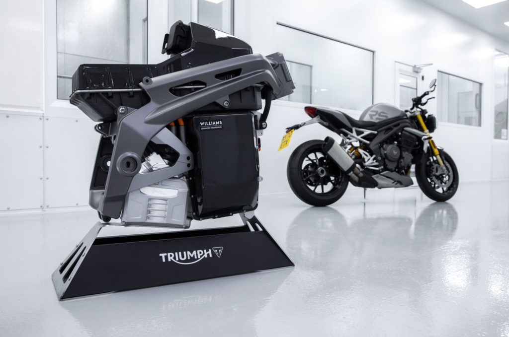 A Triumph TE-1 electric powertrain and battery pack mounted in a prototype frame with a 2021 Triumph Speed Triple 1200 RS in the background. Photo courtesy Triumph.