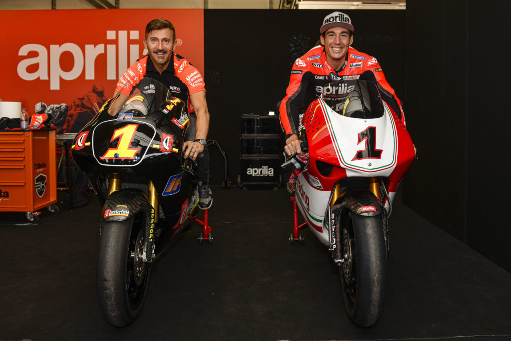 Max Biaggi (left) and Aleix Espargaro (right) seated on Biaggi’s World Championship-winning Aprilia 250s at Misano. Photo courtesy Aprilia.