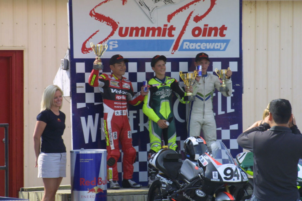 USGPRU 125 Grand Prix racer winner PJ Jacobsen (center), runner-up Nobi Iso (left), and third-place finisher Kris Turner (right) on the podium at Summit Point Raceway. Photo by etechphoto.com.