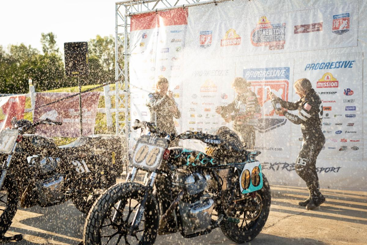 Jillian Deschenes (center), Jaycee Jones (left), and Malary Lee (right) enjoy a champagne shower on the New York Short Track AFT podium. Photo courtesy Royal Enfield North America.