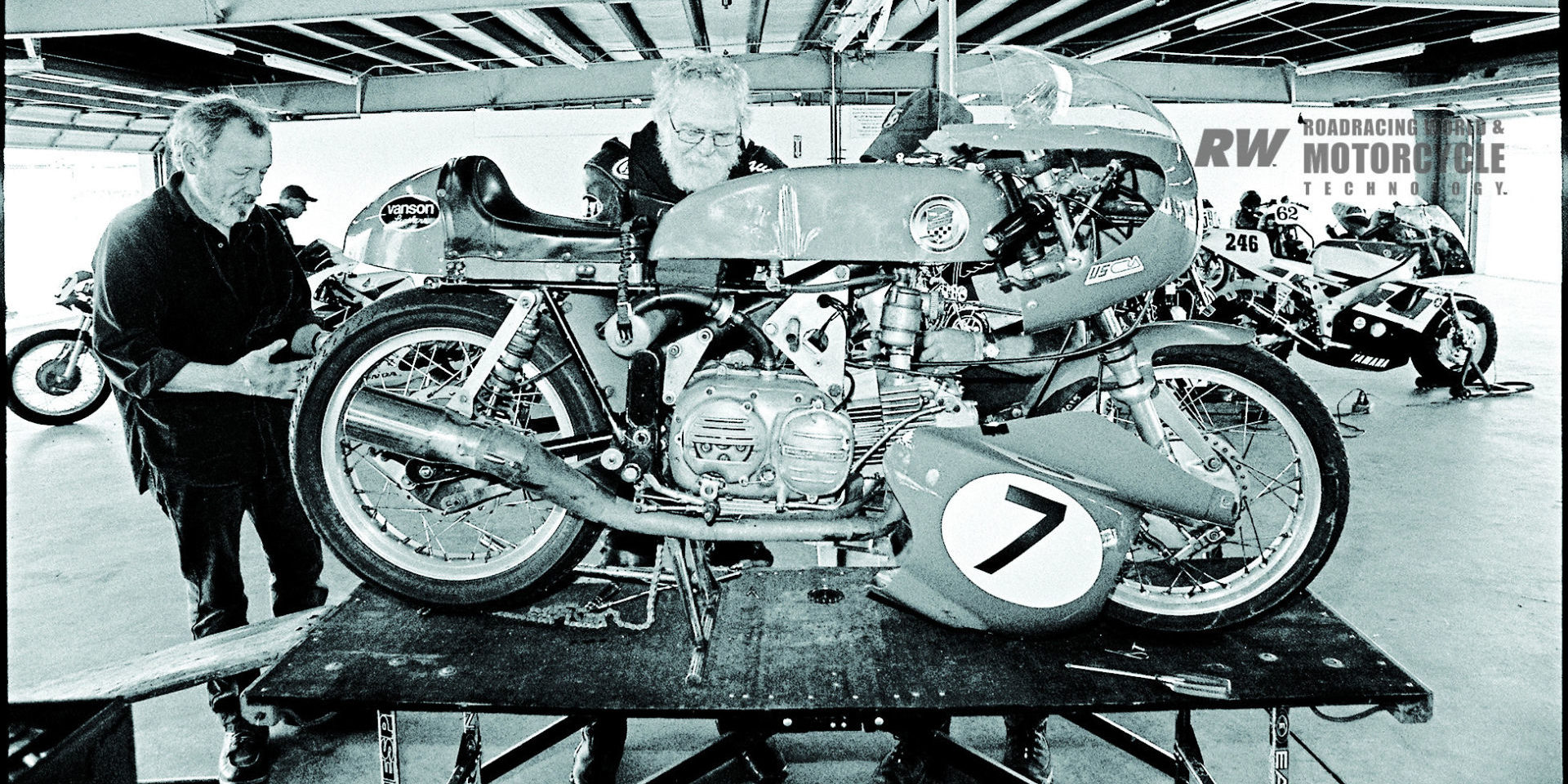 Dave Roper (center) and Gordon Pulis work on Roper’s Harley-Davidson/Aermacchi CRTT 250 Sprint racebike, in the garages. Photo by John Owens.