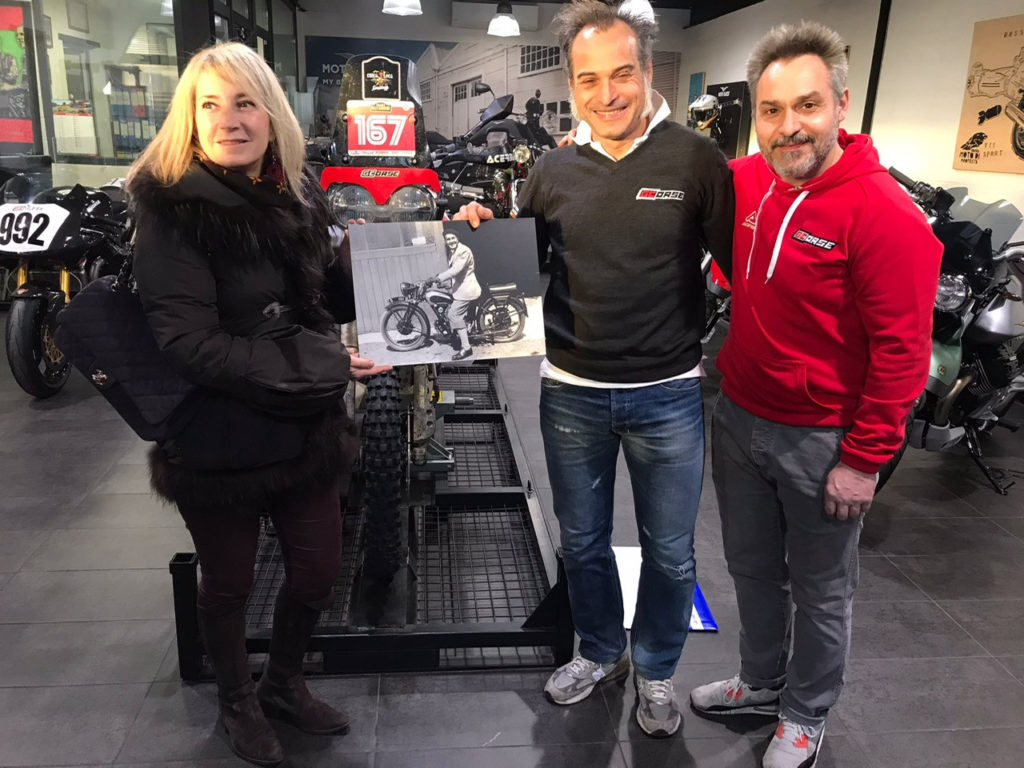 Elena Bagnasco (left) with racer and former test rider and team manager Vittoriano Guareschi (center) and his brother Gianfranco Guareschi (right) at their Moto Guzzi dealership in Parma, Italy. Bagnesco is holding a photo of her grandfather, Giorgio Parodi. Photo courtesy Elena Bagnasco.