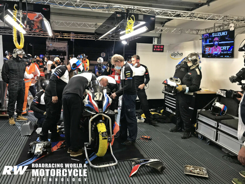As the leading Yoshimura/SERT Suzuki team is displayed on the garage monitor, the BMW team is tearing apart its stricken racebike after it ground to a halt on the circuit and was pushed back to the pits. Photo by Michael Gougis.