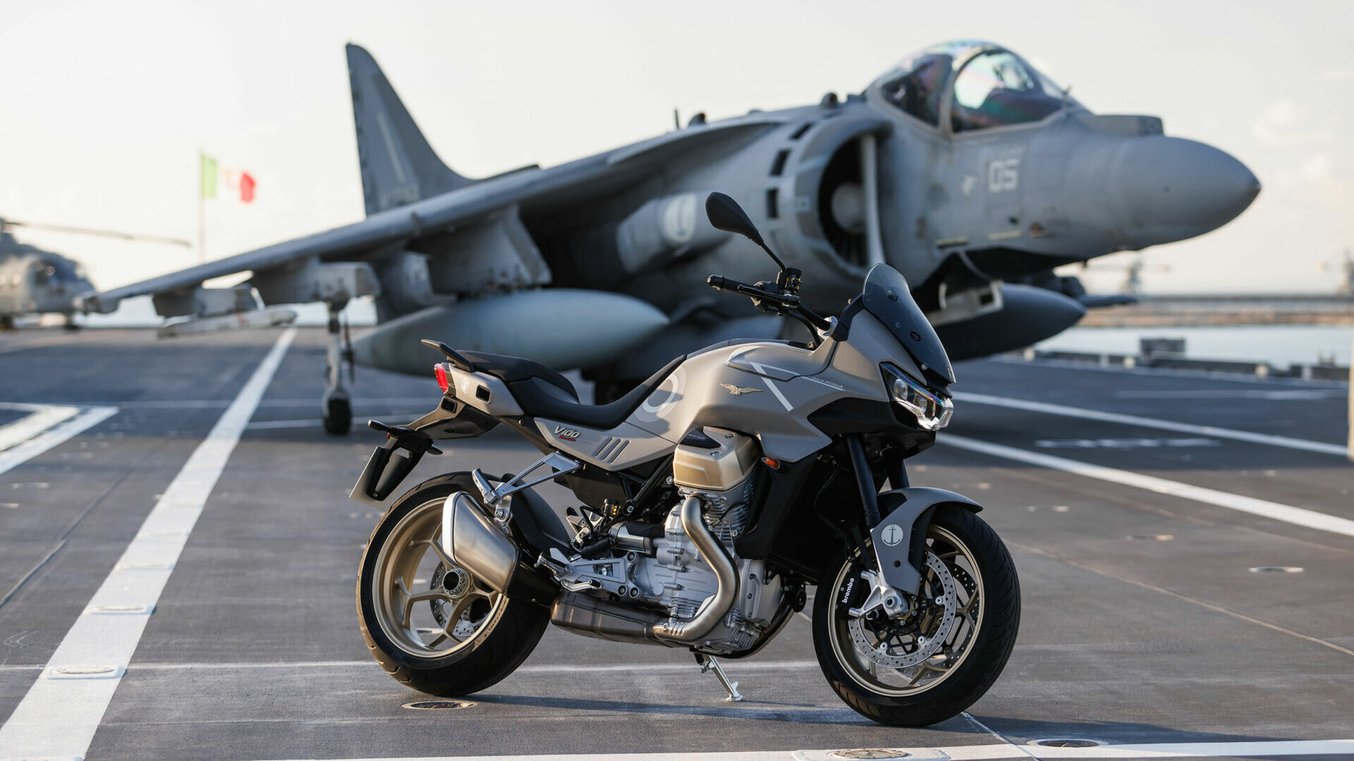 A limited-edition Moto Guzzi V100 Mandello Aviazione Navale in front of an AV-8B Harrier aircraft on the deck of the Italian aircraft carrier Cavour. Photo courtesy Moto Guzzi.