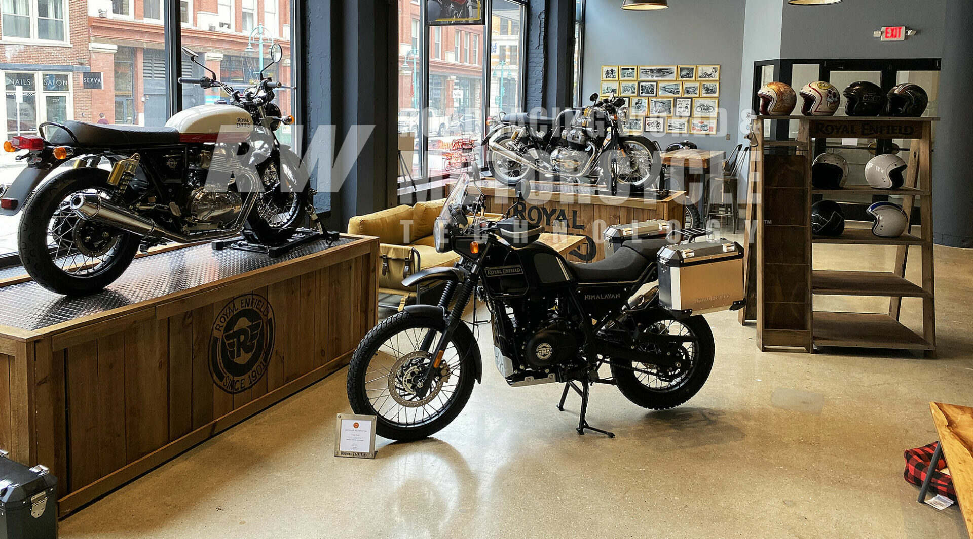 The front space on the ground floor of company headquarters is now being used as a Royal Enfield Experience venue, showcasing motorcycle models, accessories, artwork, and memorabilia. The brand's best-selling model is the 411cc single-cylinder Himalayan seen parked in the foreground, with two twin-cylinder 650cc models on display pedestals.