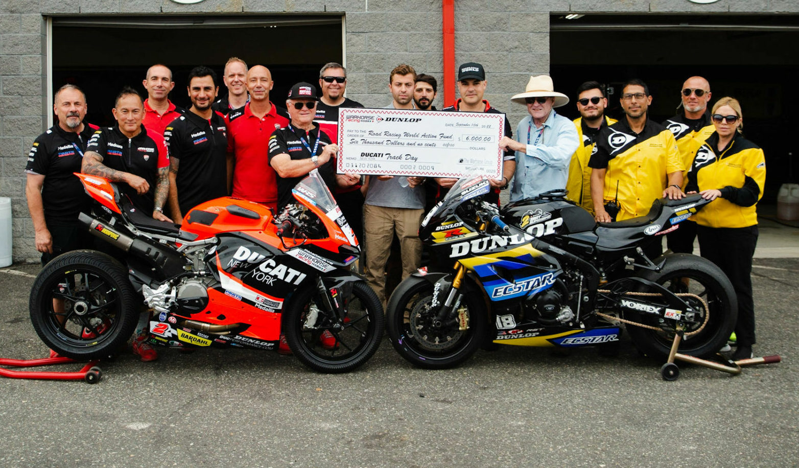 Members of the Warhorse HSBK Racing Ducati NYC race team and Dunlop’s MotoAmerica staff present a check for $6,000 to Roadracing World Action Fund (RWAF) founder John Ulrich September 11 at New Jersey Motorsports Park. Pictured (from left) are Warhorse Racing Ducati NYC race team members Maurizio Perlini, Michael Castro, Giovanni Crupi, Bobby Shek, David Behrend, Simone Toso, Eraldo Ferracci, Cody Chesebrough, Louis Denaples III, Marco Vilaro, RWAF Ambassador Chris Ulrich, RWAF Founder John Ulrich, and Dunlop’s Hunter Juico, Anthony Romo, Tom McMannis, and Cori Maynard behind Josh Herrin's Ducati Panigale V2 Supersport racebike and the Dunlop ECSTAR Suzuki GSX-R1000R two-seat Superbike, a fund-raising tool of the Roadracing World Action Fund. Photo courtesy Dunlop.