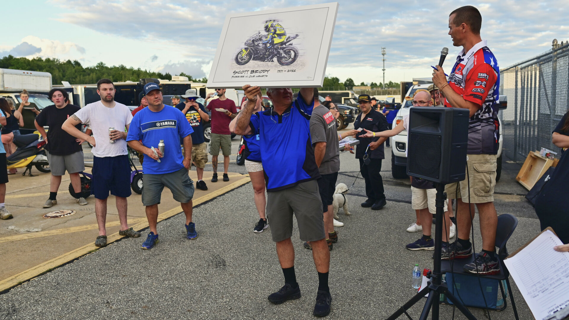 NEMRR's Eric Wood (right, with microphone) and John Grush (holding art work) at the auction to honor Scott Briody and benefit the Roadracing World Action Fund. Photo courtesy NEMRR.