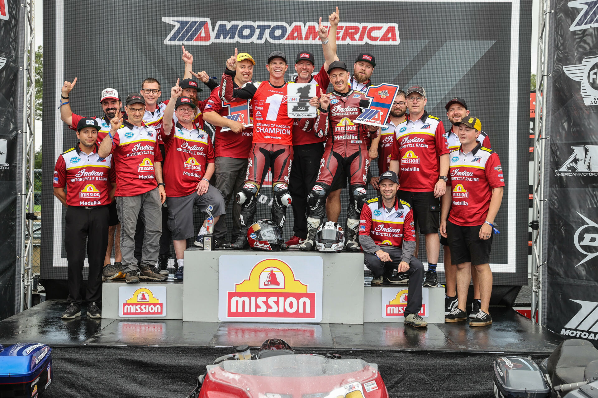 Tyler O'Hara holds up his new #1 plate and poses with teammate Jeremy McWilliams and the S&S Cycle team after winning the 2022 MotoAmerica King Of The Baggers Championship at New Jersey Motorsports Park. Indian Vice President Gary Gray is seen above the #1 plate. Photo by Brian J. Nelson.