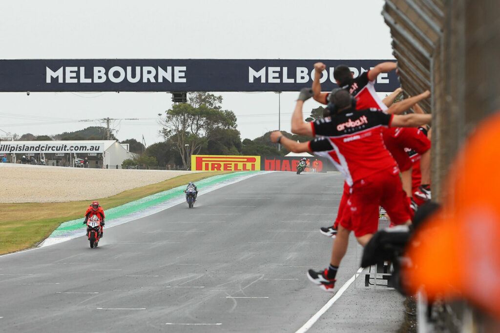 Nicolo Bulega (11) is cheered to the checkered flag by his crew lining pit wall. Photo courtesy Dorna.