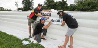 Medallia Superbike riders Mathew Scholtz (left), Jake Gagne (center), and JD Beach (right) installing a Medallia logo on a new section of soft barriers funded by Medallia. Photo by Brian J. Nelson.