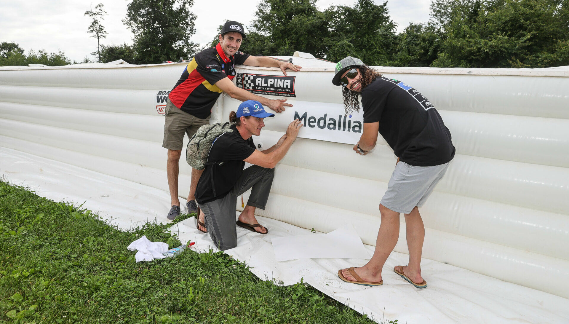 Medallia Superbike riders Mathew Scholtz (left), Jake Gagne (center), and JD Beach (right) installing a Medallia logo on a new section of soft barriers funded by Medallia. Photo by Brian J. Nelson.