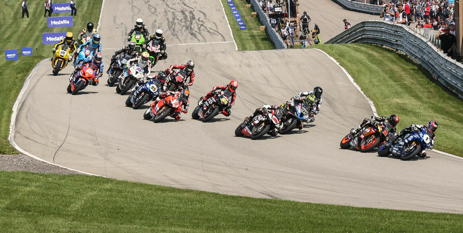 Jake Gagne (1) leads Mathew Scholtz (11), Bobby Fong (50), PJ Jacobsen (99), Cameron Beaubier (behind Jacobsen), Richie Escalante (54), Josh Herrin (2), and the rest into Turn One at Pittsburgh International Race Complex. Photo by Brian J. Nelson.