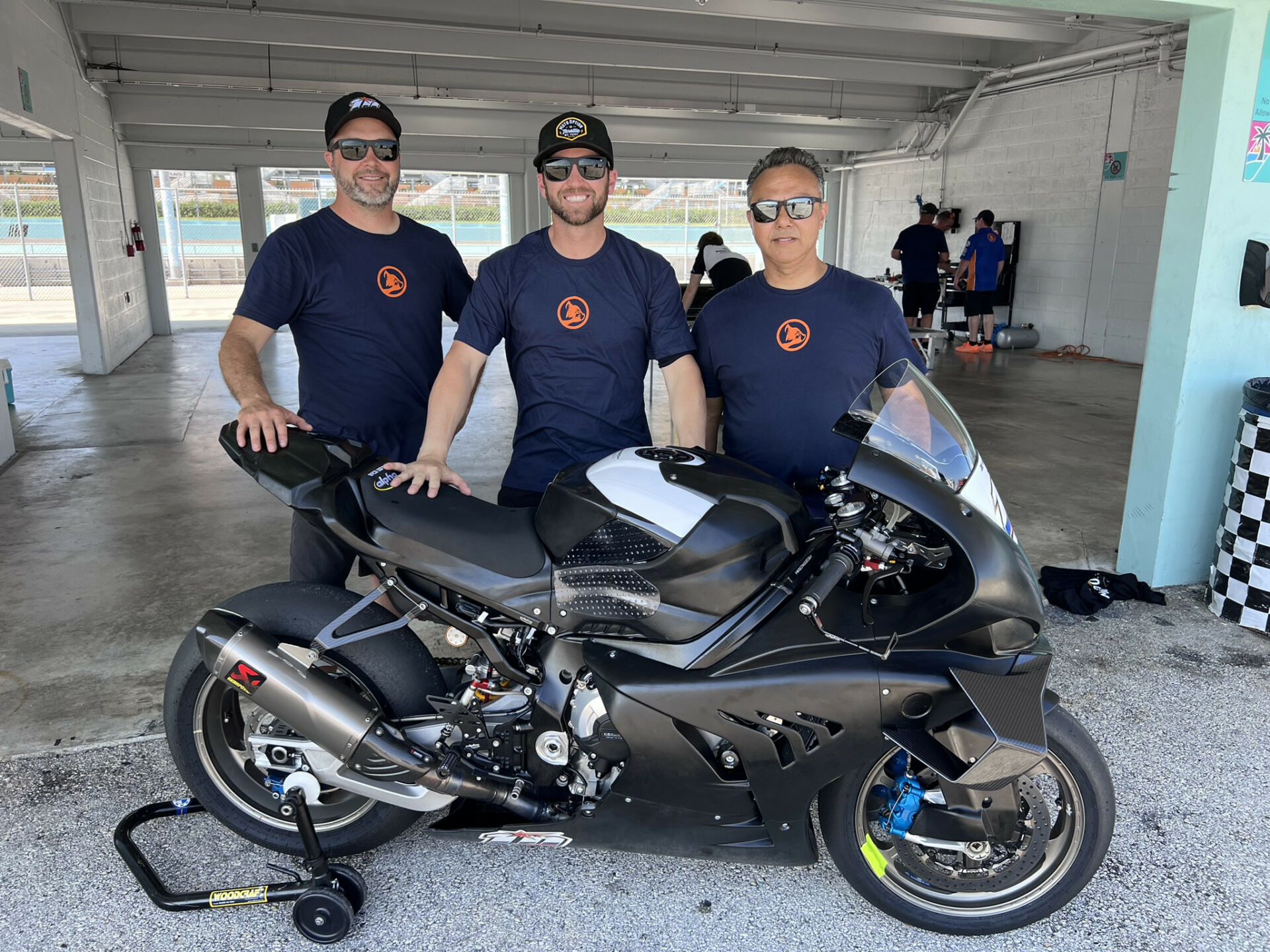 OrangeCat Racing rider Travis Wyman (center) poses with his crew chief Joel Martens (left), mechanic Alex Torres (right), and one of the team's BMW M 1000 RRs. Photo courtesy OrangeCat Racing.